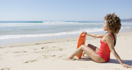 Female wearing red swimsuit with rescue float on beach looking into distance. Tarifa beach. Provincia Cadiz. Spain.