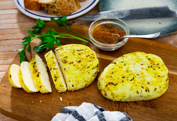 Yellow cheese with herbs and spices sliced on wooden board for serving. Lithuanian traditional cheese