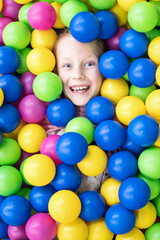 Fototapeta na wymiar Head of a laughing child peeks out of a pile of colorful balls