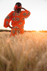 African woman in traditional clothes standing looking across field of barley or wheat crops at sunset or sunrise