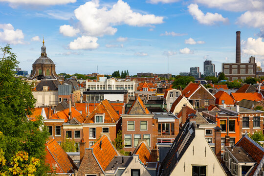 View from above of historic center of Dutch city of Leiden on sunny day overlooking typical townhouses with terracotta tiled gabled roofs, dome of St. Mary church and power station at background..
