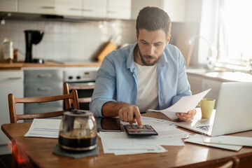 Young man going over his home finances in the kitchen - obrazy, fototapety, plakaty