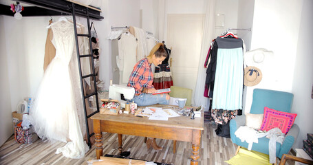 Young female in casual clothing sitting on table and using tablet on background of modern parlour.