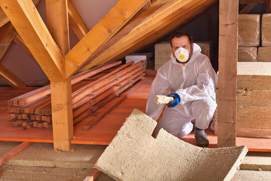 Man laying thermal insulation panels in a new house - under the roof