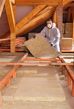 Man places rockwool thermal insulation in layers between wooden scaffolding - working in the attic of a house