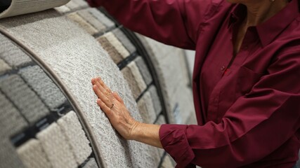 Mature woman runs hand over carpet samples shopping in large hardware store for home renovation project.