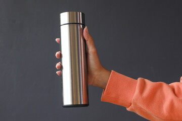 Closeup of steel eco thermo water bottle in female hand on dark grey background