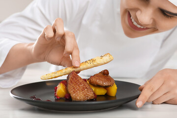 Professional chef decorating delicious dish with crispy bread at marble table, closeup