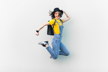 Portrait of attractive overjoyed hipster woman in blue denim overalls, yellow T-shirt and black...