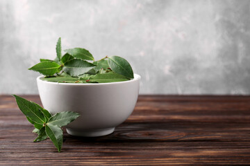 Fresh green bay leaves in bowl on wooden table, closeup. Space for text