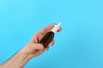 Man holding nasal spray on light blue background, closeup. Space for text