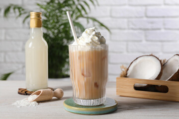 Bottle of delicious syrup, glass of iced coffee, halves of coconut and flakes on white wooden table