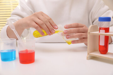 Girl mixing colorful liquids at white table indoors, closeup. Chemical experiment set for kids