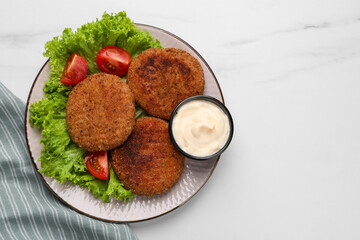 Plate with delicious vegan cutlets, lettuce, tomatoes and sauce on white marble table, top view. Space for text