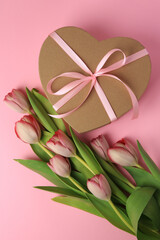Heart shaped gift box with bow and beautiful tulips on pale pink background, flat lay