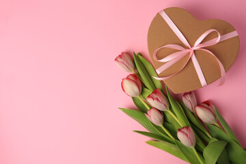 Fototapeta na wymiar Heart shaped gift box with bow and beautiful tulips on pale pink background, flat lay. Space for text