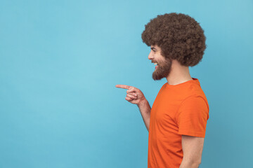 Side view of man with Afro hairstyle wearing orange T-shirt pointing finger away with toothy smile...