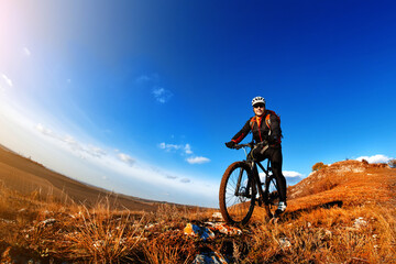 Fototapeta na wymiar Mountain Bike and blue sky background. photographed on a fisheye lens. Cyclist in the helmet. Landscape with hill, mound and blue sky. Countryside.