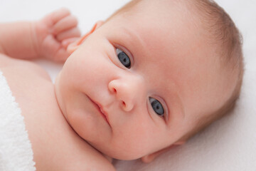 Cute adorable newborn baby in white bed and wrapped in blanket and looking at the camera