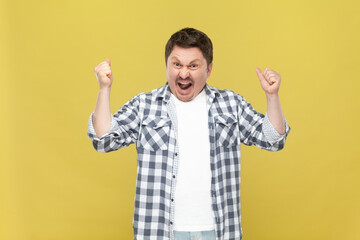 Extremely happy overjoyed middle aged man in casual checkered shirt standing with raised arms and...