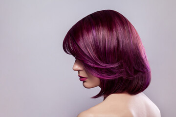 Side view portrait of beautiful fashion model woman with short purple colored hairstyle, looking away, showing her bright stylish colour of hair. Indoor studio shot isolated on gray background.