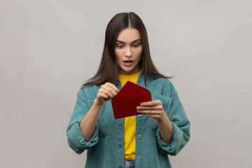 Portrait of amazed surprised woman holding red romantic envelope and looking at letter with open...