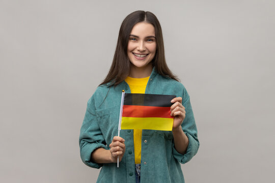 Portrait of attractive woman holding Germany flag, celebrating Day of Germany - 3th October, expressing positive emotions, wearing casual style jacket. Indoor studio shot isolated on gray background.