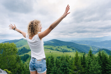 Fototapeta premium Young woman standing on cliff's edge and looking to a sky with raised hands
