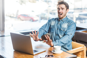 Portrait of shocked panicked scared young man freelancer in blue jeans shirt working on laptop,...