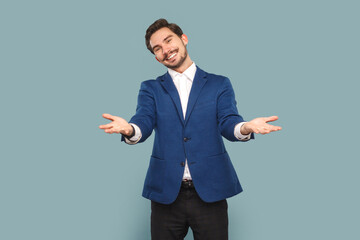 Portrait of friendly positive man with mustache standing with spread hands, saying welcome, take for free, wearing white shirt and jacket. Indoor studio shot isolated on light blue background.