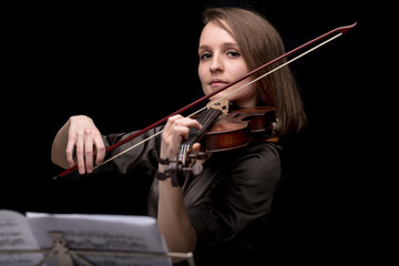 Young beautiful woman violinist player playing her instrument on her shoulder holding bow. portrait in a blurred dark room in background. Concept of classical music