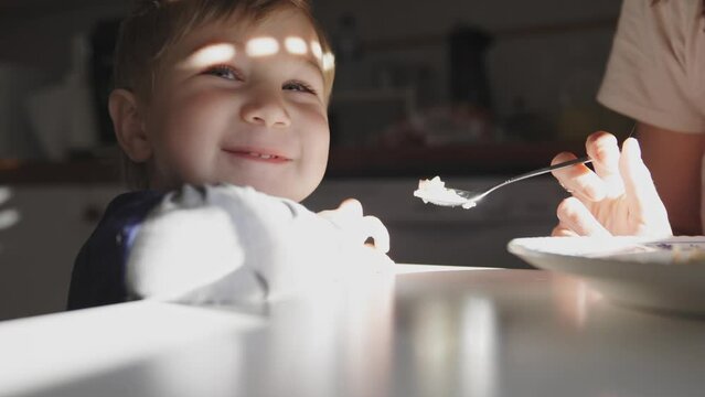Mother feeds her little smiling son from spoon