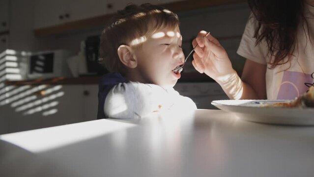 Mom feeds her cute son from spoon in morning