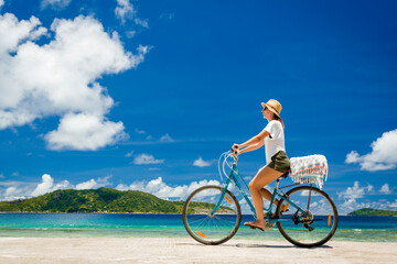 Fototapeta na wymiar Woman on a bicycle ride along The Beach at Seychelles
