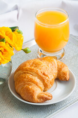 Morning breakfast with croissant and orange juice in glass, yellow roses  on vintage silver tray.