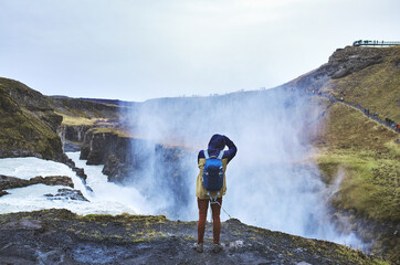 A man stands on the edge of a waterfall Gullfoss and takes pictures of him. Cloudy autumn day. Traveling in autumn in Iceland