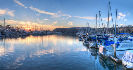 Fototapeta na wymiar Sunset over sailboats in the calm water of the Dana Point harbor in Southern California, USA