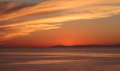 Fototapeta na wymiar Orange sunset over Catalina Island in a calm ocean in Laguna Beach, Southern California, United States