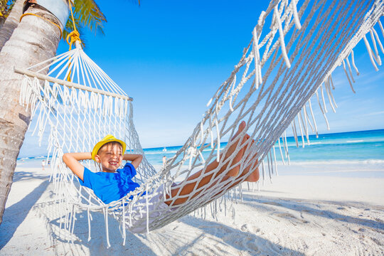 Cheerful little boy relaxing on a tropical beach in hammock.