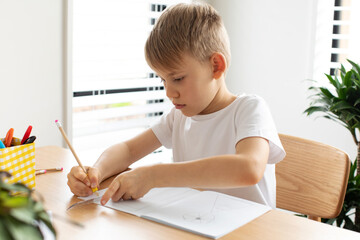 A cute boy makes a drawing with a ruler and pencil. Home lessons. Geometry and drawing.