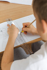 A cute boy makes a drawing with a ruler and pencil. Home lessons. Geometry and drawing.