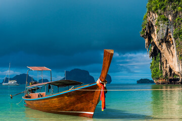 Fototapeta na wymiar A Thai boat with a long tail near the shore, a blue rain cloud over the Andaman Sea