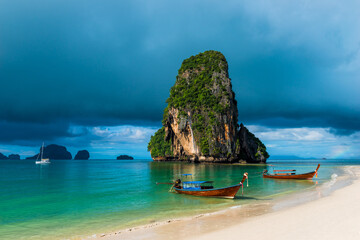 Fototapeta na wymiar high rock in the sea, rain cloud and Thai boats near the shore