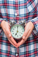 Close-up of an alarm clock in female hands on a background of pajamas