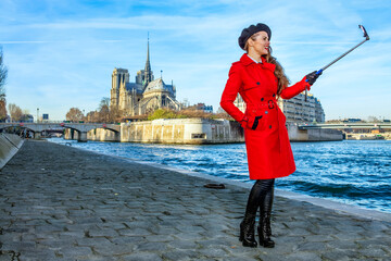 Bright in Paris. smiling elegant tourist woman in red trench coat on embankment near Notre Dame de...