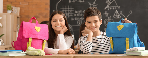Little students with backpacks sitting at desks in classroom