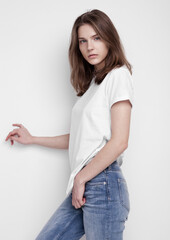 Model test portrait with young beautiful fashion model posing on grey background. Wearing white t-shirt and jeans.