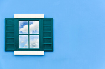 Sky and cloud reflection in green window glass on blue wall of house, Italy retro style
