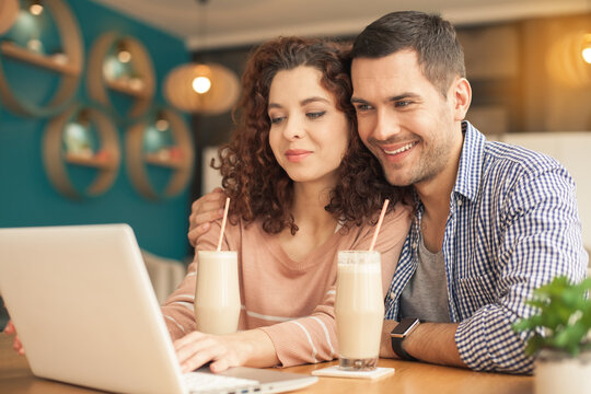 Date in cafe. Lovely couple in cafe with stylish interior. Man and woman having delicious coffee drinks. They chatting, using laptop and smiling