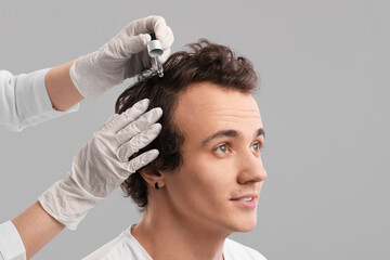 Young man receiving serum for hair growth on grey background, closeup